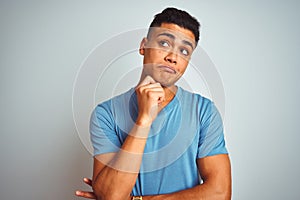 Young brazilian man wearing blue t-shirt standing over isolated white background with hand on chin thinking about question,