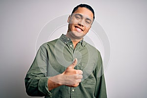 Young brazilian man wearing casual shirt standing over isolated white background doing happy thumbs up gesture with hand