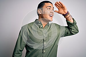 Young brazilian man wearing casual shirt standing over isolated white background very happy and smiling looking far away with hand