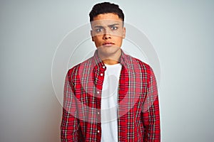 Young brazilian man wearing red shirt standing over isolated white background skeptic and nervous, disapproving expression on face