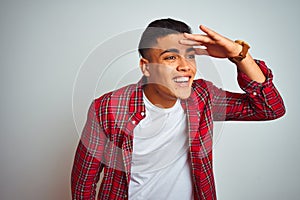 Young brazilian man wearing red shirt standing over isolated white background very happy and smiling looking far away with hand