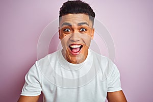 Young brazilian man wearing t-shirt standing over isolated pink background very happy and excited, winner expression celebrating