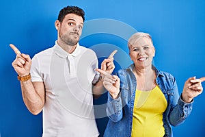Young brazilian mother and son standing over blue background smiling confident pointing with fingers to different directions