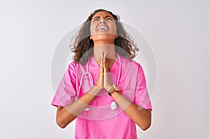 Young brazilian nurse woman wearing stethoscope standing over  white background begging and praying with hands together