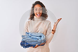 Young brazilian shopkeeper woman holding pile of jeans over isolated white background very happy and excited, winner expression