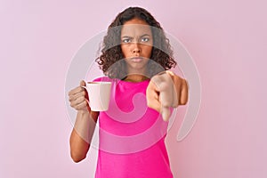 Young brazilian woman drinking cup of coffee standing over isolated pink background pointing with finger to the camera and to you,