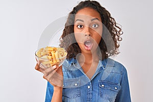 Young brazilian woman holding bowl with macaroni pasta over isolated white background scared in shock with a surprise face, afraid