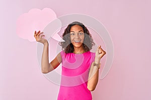 Young brazilian woman holding cloud speech bubble standing over isolated pink background happy with big smile doing ok sign, thumb