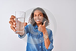 Young brazilian woman holding glass of water standing over isolated white background happy with big smile doing ok sign, thumb up