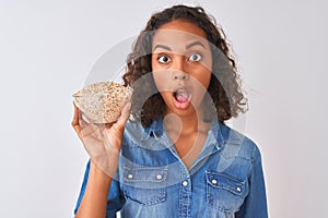 Young brazilian woman holding oat bowl standing over isolated white background scared in shock with a surprise face, afraid and