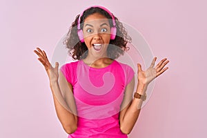 Young brazilian woman listening to music using headphones over isolated pink background very happy and excited, winner expression