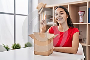 Young brazilian woman looking inside cardboard box smiling with an idea or question pointing finger up with happy face, number one