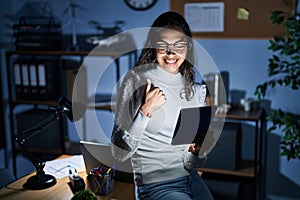 Young brazilian woman using touchpad at night working at the office doing happy thumbs up gesture with hand