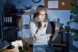 Young brazilian woman using touchpad at night working at the office feeling unwell and coughing as symptom for cold or bronchitis