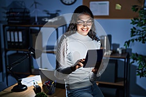 Young brazilian woman using touchpad at night working at the office with a happy and cool smile on face