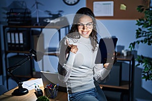 Young brazilian woman using touchpad at night working at the office looking confident with smile on face, pointing oneself with