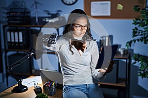 Young brazilian woman using touchpad at night working at the office looking unhappy and angry showing rejection and negative with