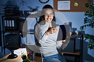 Young brazilian woman using touchpad at night working at the office smiling friendly offering handshake as greeting and welcoming