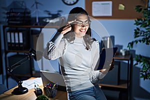 Young brazilian woman using touchpad at night working at the office smiling pointing to head with one finger, great idea or