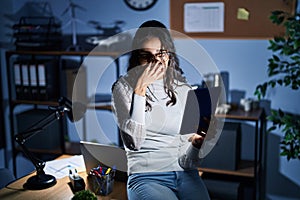Young brazilian woman using touchpad at night working at the office tired rubbing nose and eyes feeling fatigue and headache