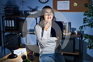 Young brazilian woman using touchpad at night working at the office touching painful neck, sore throat for flu, clod and infection