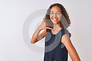 Young brazilian woman wearing blue dress standing over isolated white background smiling doing phone gesture with hand and fingers