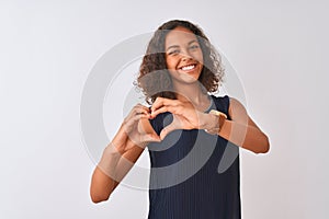 Young brazilian woman wearing blue dress standing over isolated white background smiling in love doing heart symbol shape with