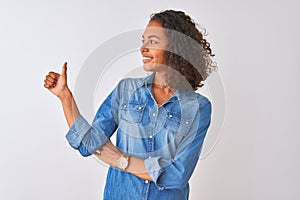 Young brazilian woman wearing denim shirt standing over isolated white background Looking proud, smiling doing thumbs up gesture
