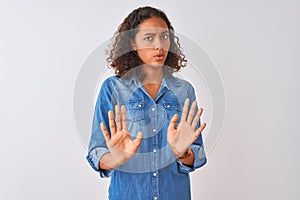 Young brazilian woman wearing denim shirt standing over isolated white background Moving away hands palms showing refusal and