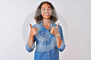 Young brazilian woman wearing denim shirt standing over isolated white background success sign doing positive gesture with hand,