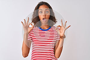 Young brazilian woman wearing red striped t-shirt standing over isolated white background looking surprised and shocked doing ok