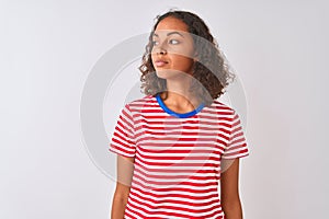 Young brazilian woman wearing red striped t-shirt standing over isolated white background smiling looking to the side and staring