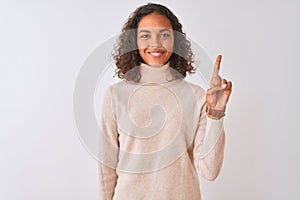 Young brazilian woman wearing turtleneck sweater standing over isolated white background showing and pointing up with finger