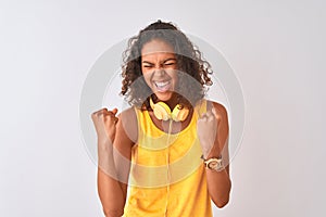 Young brazilian woman wearing yellow headphones over isolated white background very happy and excited doing winner gesture with