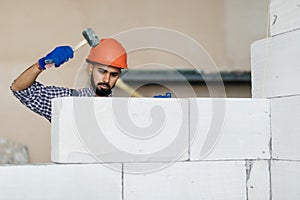 Young bricklayer builder working with autoclaved aerated concrete blocks. Walling, installing bricks on construction site