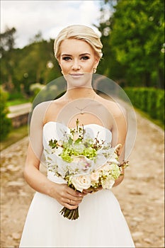 Young bride, beautiful blonde, model girl with blue eyes with flowers in the hands, outdoors