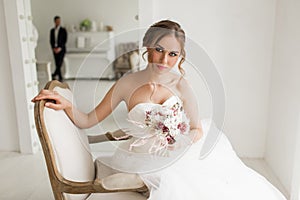 Young bride in a beautiful dress holding a bouquet of flowers in bright white studio. Wedding concept.