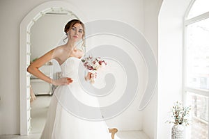 Young bride in a beautiful dress holding a bouquet of flowers in bright white studio. Wedding concept.