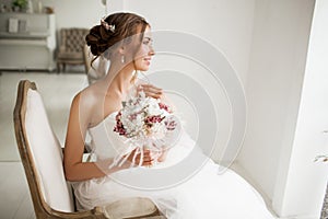 Young bride in a beautiful dress holding a bouquet of flowers in bright white studio. Wedding concept.