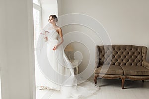 Young bride in a beautiful dress holding a bouquet of flowers posing near window in bright white studio. Wedding concept
