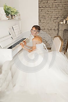 Young bride in a beautiful dress is playing piano in bright white studio. Wedding concept.