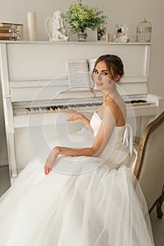 Young bride in a beautiful dress is playing piano in bright white studio. Wedding concept.