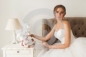 Young bride in a beautiful dress sitting at home with nice white interior. Wedding concept.