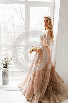 Young bride in a beautiful dress and wreath on her head holding a bouquet of flowers in bright white studio. Wedding