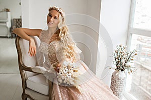 Young bride in a beautiful dress and wreath on her head holding a bouquet of flowers in bright white studio. Wedding