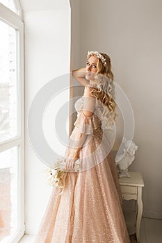 Young bride in a beautiful dress and wreath on her head holding a bouquet of flowers in bright white studio. Wedding