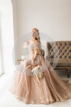 Young bride in a beautiful dress and wreath on her head holding a bouquet of flowers in bright white studio. Wedding