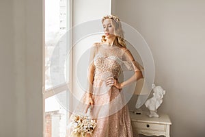 Young bride in a beautiful dress and wreath on her head holding a bouquet of flowers in bright white studio. Wedding