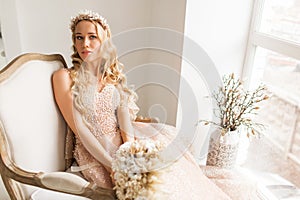 Young bride in a beautiful dress and wreath on her head holding a bouquet of flowers in bright white studio. Wedding
