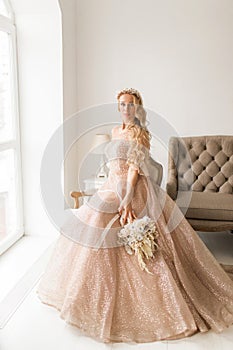 Young bride in a beautiful dress and wreath on her head holding a bouquet of flowers in bright white studio. Wedding